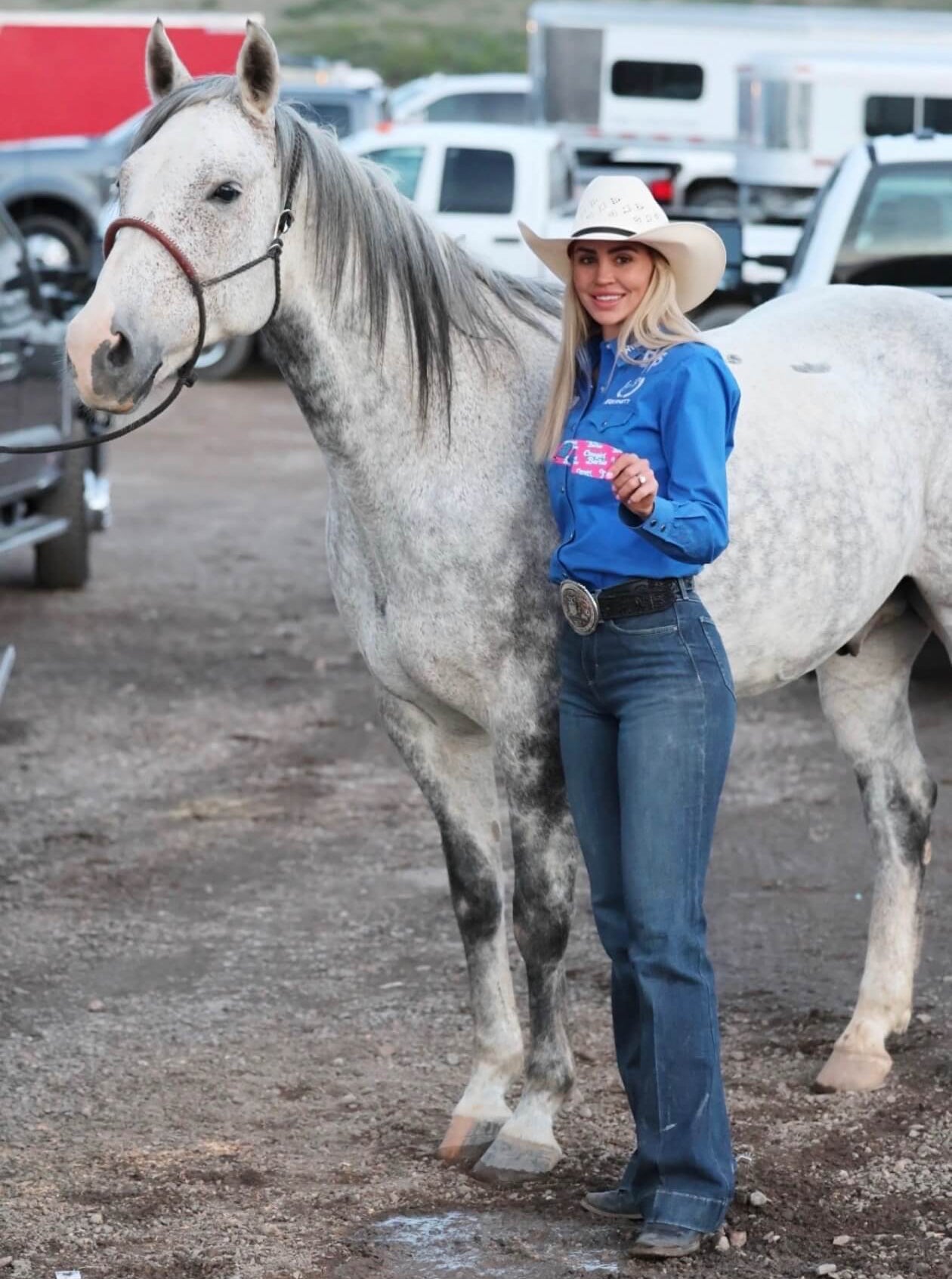 cowgirl standing with grey horse and pink hat cinch